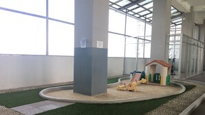 Zona de juegos infantiles con un arenero y una casita pequeña, rodeada de césped artificial y guijarros.