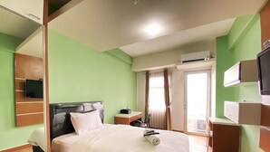 Una habitación de hotel con cama, escritorio, silla, televisor y aire acondicionado.