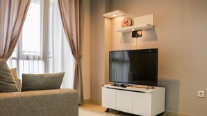 A modern living room with a flat-screen TV, a white entertainment unit, and a large window with curtains. - Nice And Comfy 2Br Apartment At Royal Olive Residence (Jakarta)