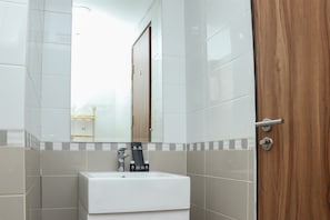 A bathroom with a white sink, a mirror, and a wooden door. - Nice And Comfy 2Br Apartment At Royal Olive Residence (Jakarta)