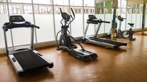 Un gimnasio con cuatro cintas de correr, ventanas amplias y suelo de madera.