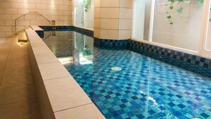 Una piscina con azulejos azules y blancos, una barandilla de cristal y una pared revestida con azulejos y una ventana.