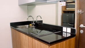 Una cocina moderna con encimera negra, pileta de acero inoxidable y microondas integrado.