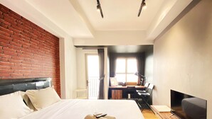 A hotel room with a large bed, a desk with a chair, a television, and a brick wall.