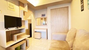 A modern living room with a flat-screen TV, built-in shelves, a white sofa, and a small ottoman. - Relaxing 1Br At Apartment At Newton Residence Bandung (Bandung)