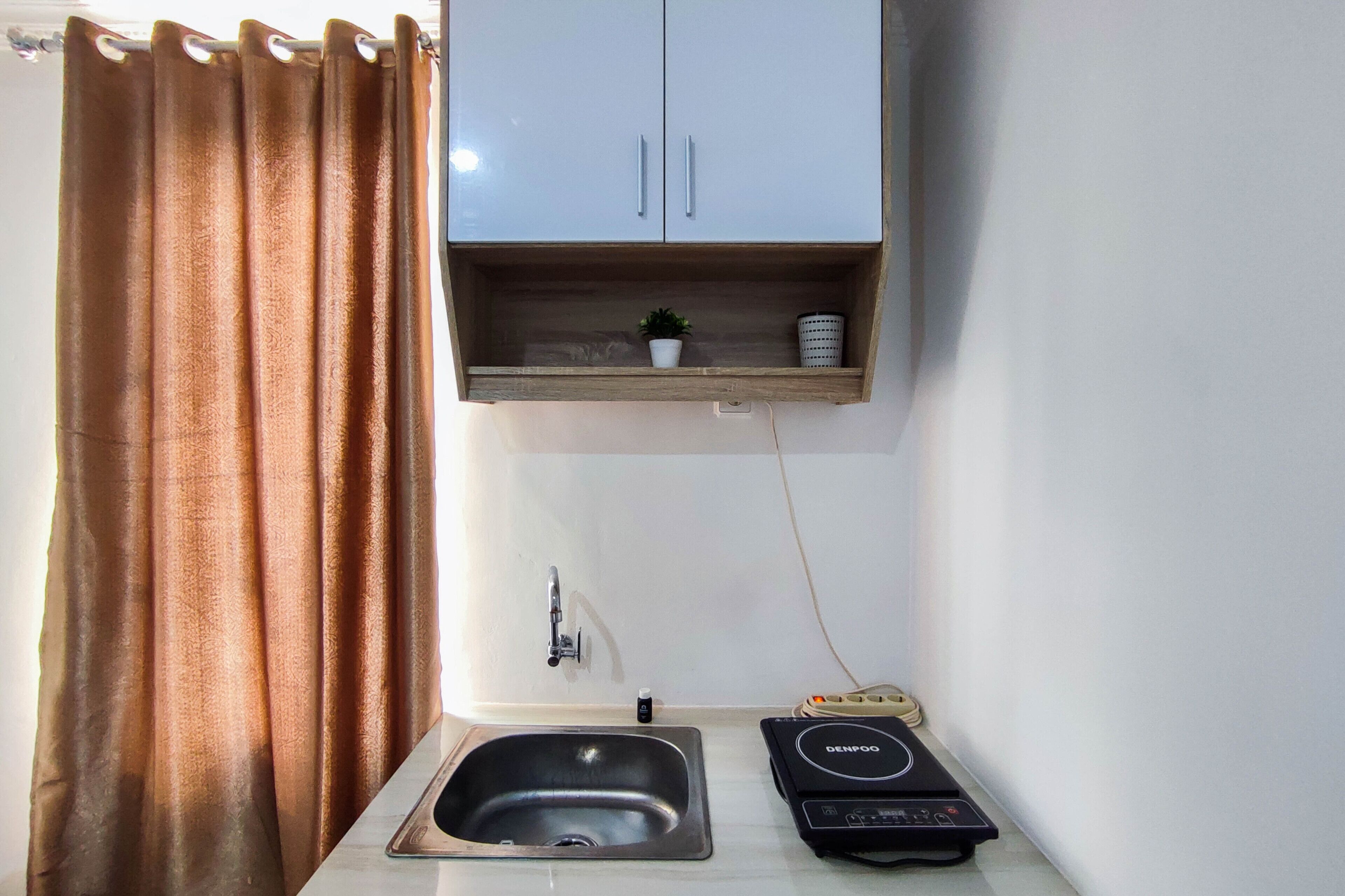 A small bathroom with a shower curtain, a sink, a cabinet above the sink, and a hairdryer on the floor.