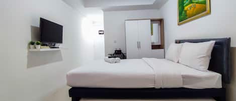 Un dormitorio con cama, televisor, armario y un cuadro en la pared.
