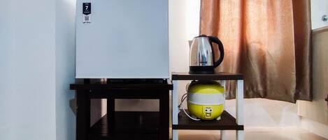 A compact kitchenette with a white refrigerator, a coffee maker, and a yellow rice cooker on a small table.