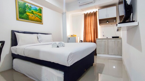 Un dormitorio ordenado con cama, kitchenette y un cuadro en la pared.