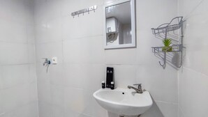 Un baño con un lavamanos blanco, un espejo, un perchero para toallas y un pequeño estante con una planta.