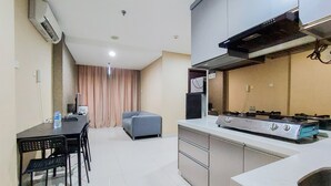 A compact kitchen with a gas stove, a refrigerator, and a dining area with chairs and a table. - Stunning And Spacious 2Br Brooklyn Alam Sutera Apartment (South Tangerang)