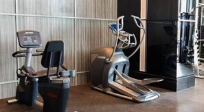 Een fitnessruimte met cardiotoestellen, waaronder een loopband en een elliptische trainer, voor een muur met een gestreept patroon.