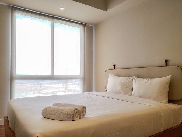 A bedroom with a large window, a bed with white linens, and a wooden headboard. - Simple And Cozy Designed 2Br Apartment At Tokyo Riverside Pik 2 (Teluknaga)
