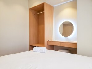 A bedroom with a bed, a wooden wardrobe, a vanity with a mirror, and a towel on the bed. - Simple And Cozy Designed 2Br Apartment At Tokyo Riverside Pik 2 (Teluknaga)