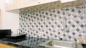 A kitchen with a black countertop, a stainless steel sink, and a patterned backsplash. - Cozy Studio At Urbantown Serpong Apartment (South Tangerang)