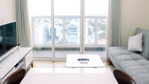 Une chambre d’hôtel moderne dotée d’un grand balcon, d’un téléviseur à écran plat, d’une table basse blanche et d’un canapé gris.