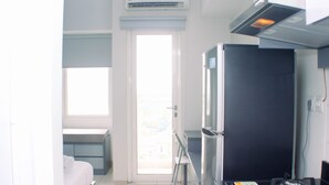A compact hotel room with a bed, a small desk, a refrigerator, and a window with a view. - Good Deal And Comfy Studio Apartment Springlake Summarecon Bekasi (Bekasi)