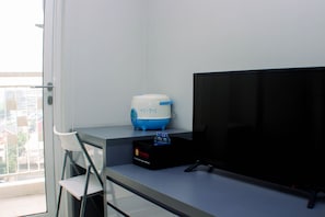 Een moderne kamer met een grote flatscreen-tv, een kleine witte stoel, een blauw-witte speaker en een zwart doosje met een rood logo op een tafel.