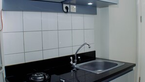 A kitchen with a black countertop, stainless steel sink, and a gas stove. - Good Deal And Comfy Studio Apartment Springlake Summarecon Bekasi (Bekasi)