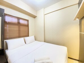 Hotellihuone, jossa on sänky, ikkuna, jossa on sälekaihtimet, ja seinä, jossa on valokatkaisin.