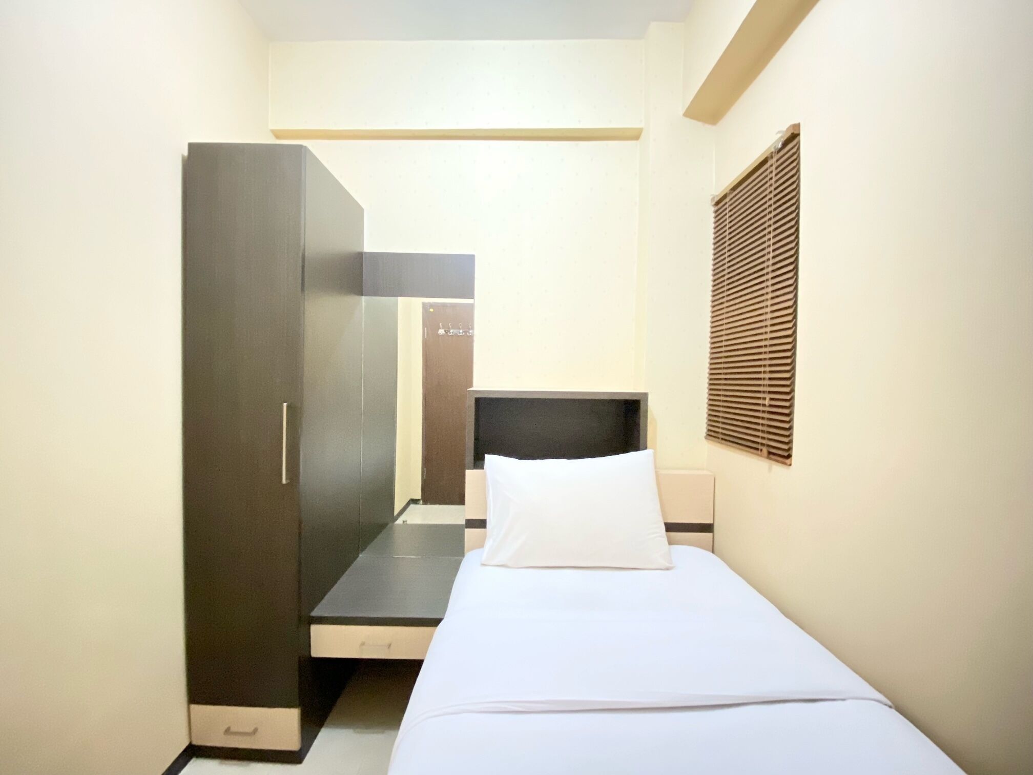 A small, compact room with a bed, a wardrobe, and a desk.