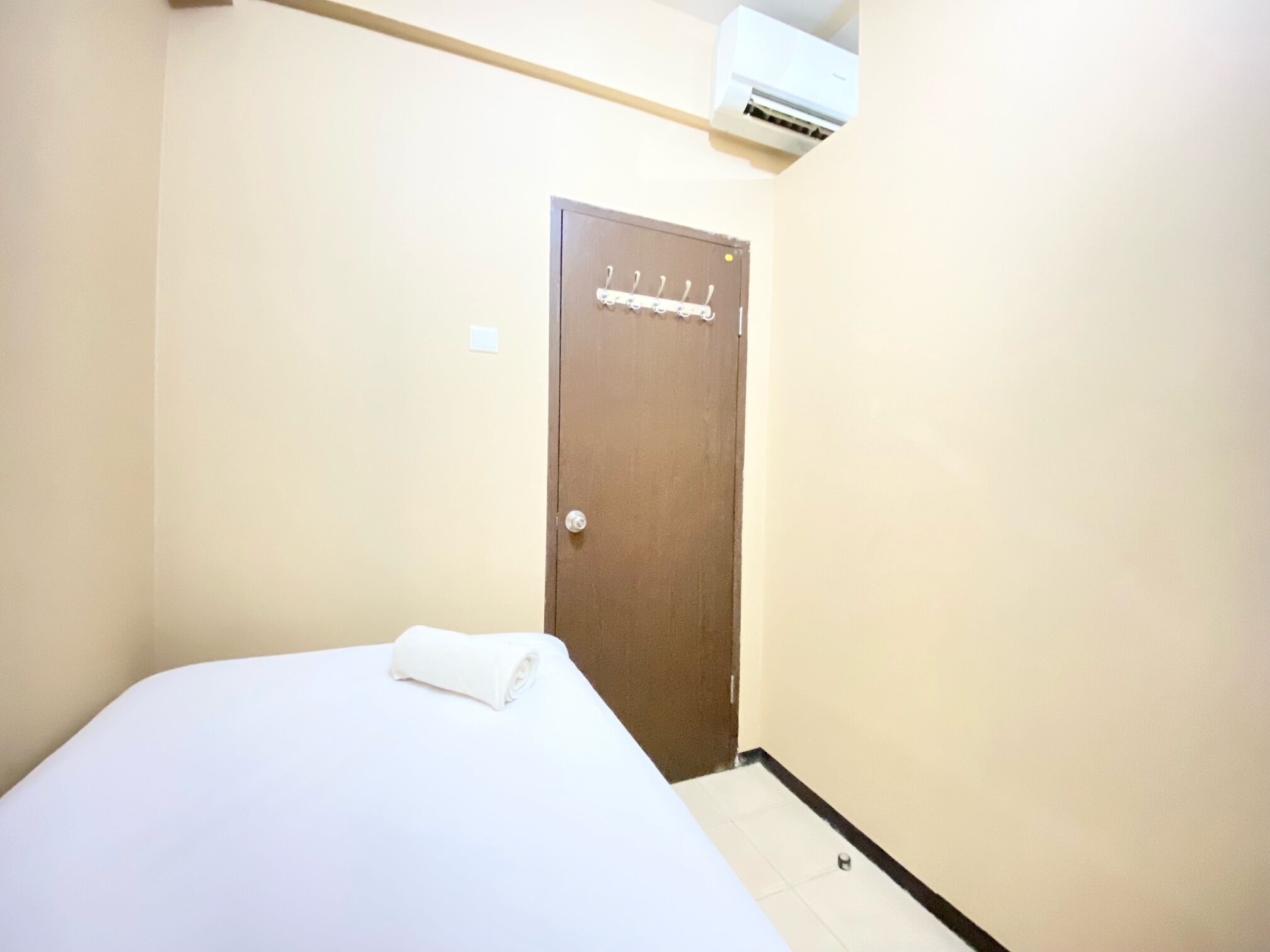 Habitación de hotel con cama, una puerta con perchero y un equipo de aire acondicionado sobre la puerta.