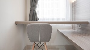 Una silla con respaldo gris y patas de madera, ubicada frente a una ventana con cortina, sobre un muro con panel de madera clara y una estantería.