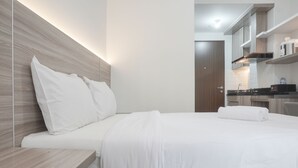 Una habitación de hotel moderna con cabecera de madera, una cama bien hecha, una pequeña mesa de madera y una zona de kitchenette.