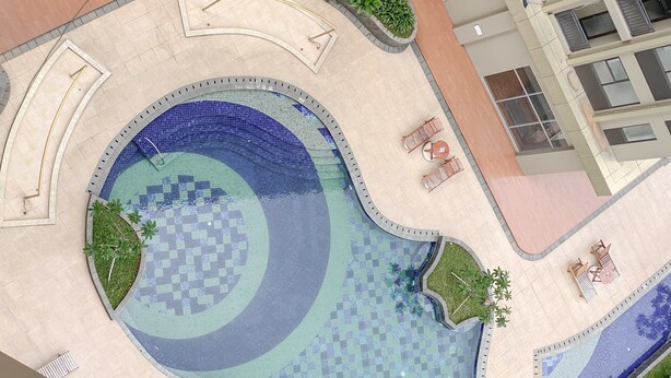 Una piscina en la azotea con diseño de cuadros, rodeada de sillones de descanso y pequeñas plantas.