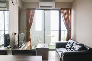 Un salon comprenant un téléviseur, un canapé, une table basse et une porte-fenêtre coulissante donnant sur un balcon.