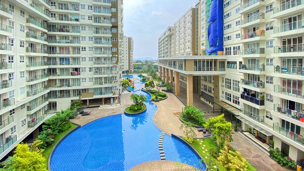 Un moderno complejo de apartamentos con piscina central, varios balcones y exuberante jardinería.