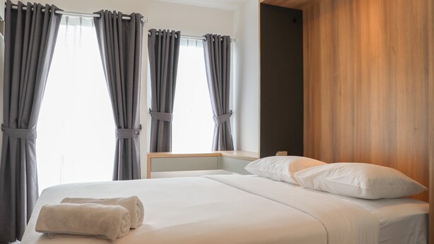 A hotel room with a bed, grey curtains, and a wooden headboard. - Well Furnished Studio At Citra Living Apartment By Tarvelio (Jakarta)