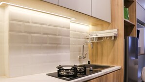 A modern kitchen with white subway tiles, a gas stove, a stainless steel sink, wooden cabinets, and a built-in oven. - Well Furnished Studio At Citra Living Apartment By Tarvelio (Jakarta)