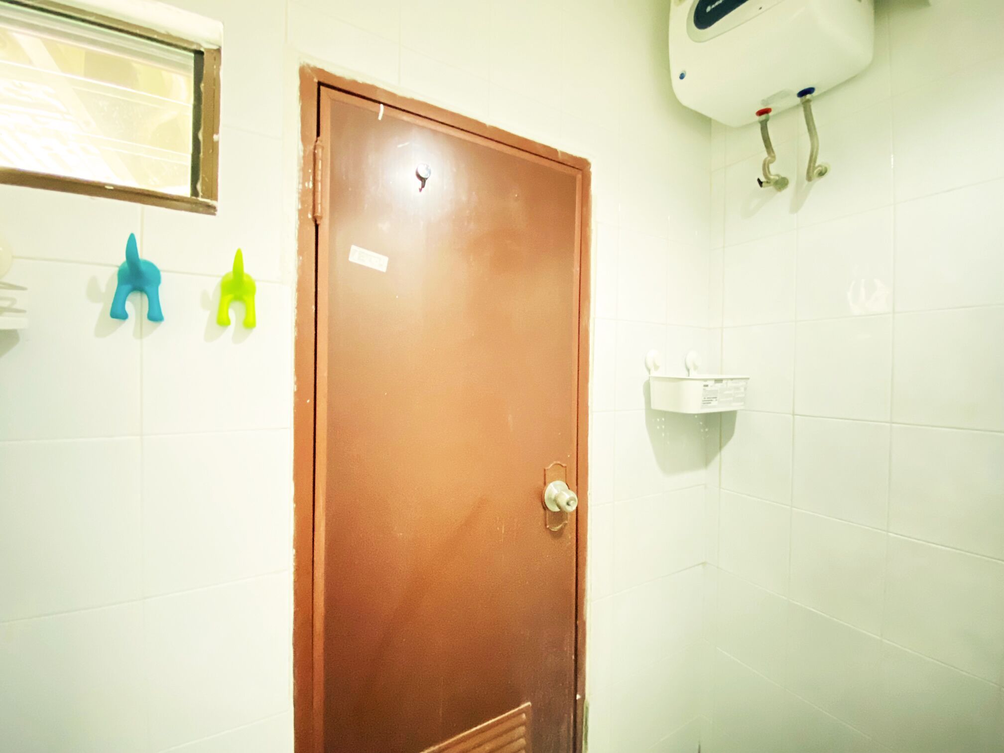 A bathroom with a brown door, white tiles, a small sink, and colorful soap dispensers.