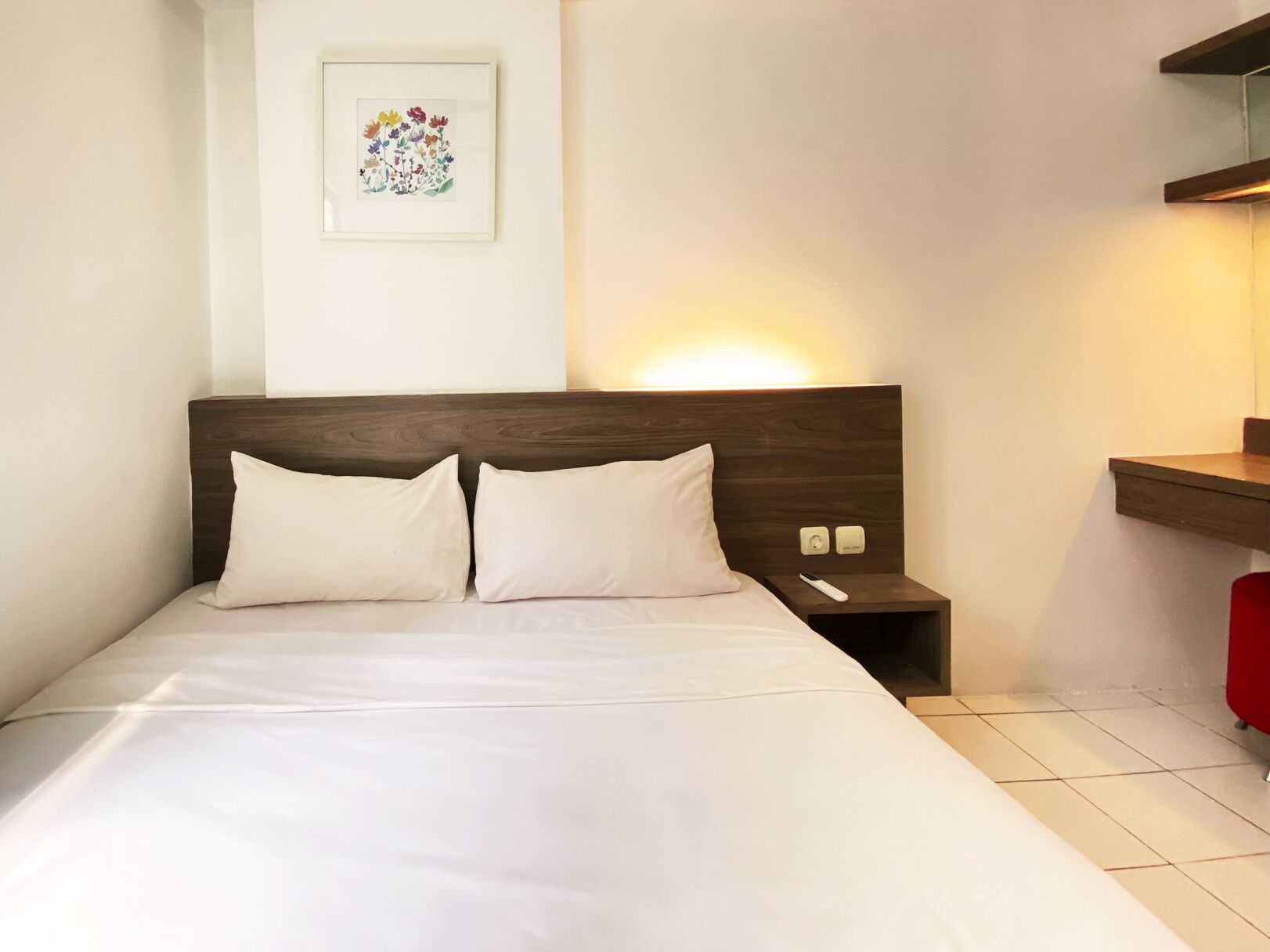 A neatly made bed with two pillows, a bedside table with a lamp, and a framed artwork on the wall.