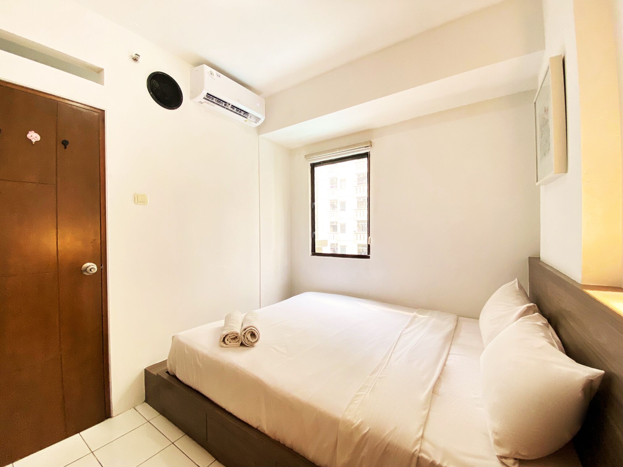 A bedroom with a bed, a window, an air conditioning unit, and a door.