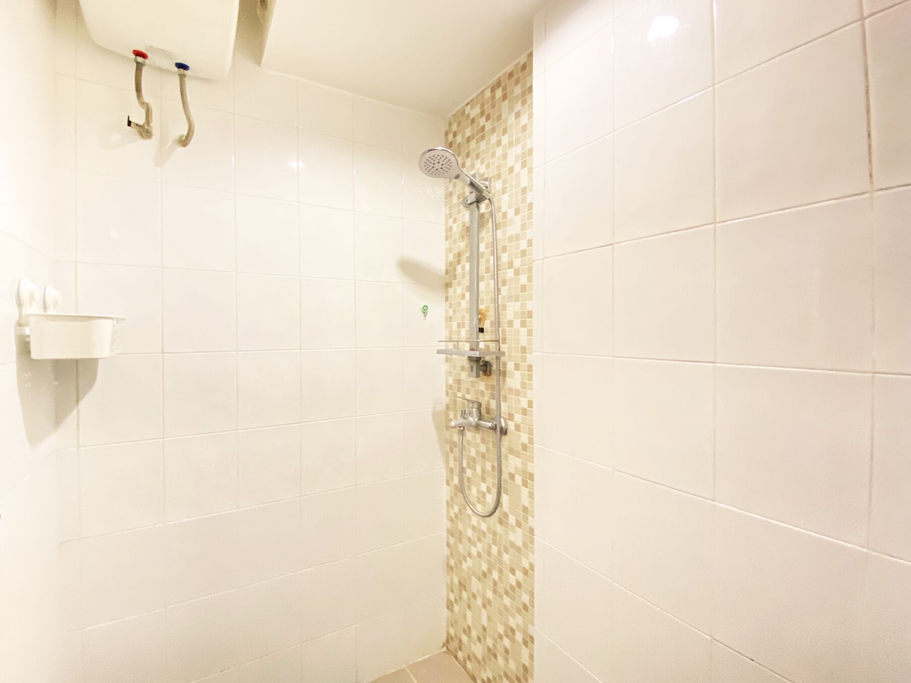 A bathroom with white tiles, a shower with a handheld showerhead, and a soap dispenser on the wall.