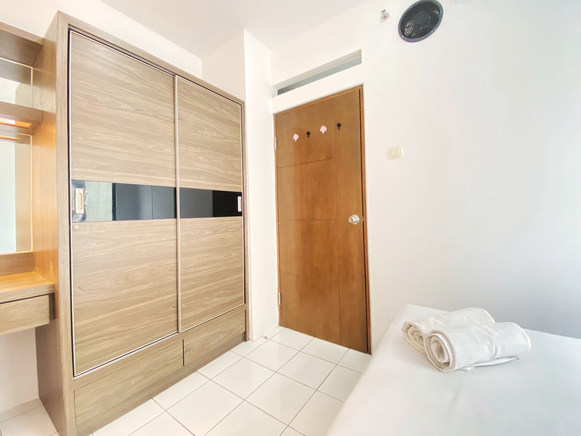 A modern bedroom with a wooden wardrobe, a wooden door, and a neatly made bed with a rolled white towel.