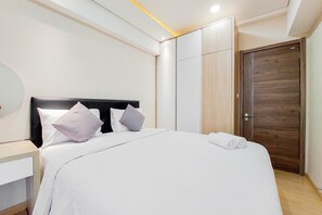 A neatly made bed with white bedding and two pillows, a wooden wardrobe, and a wooden door. - Well Designed And Comfy 2Br Sky House Bsd Apartment (Pagedangan)