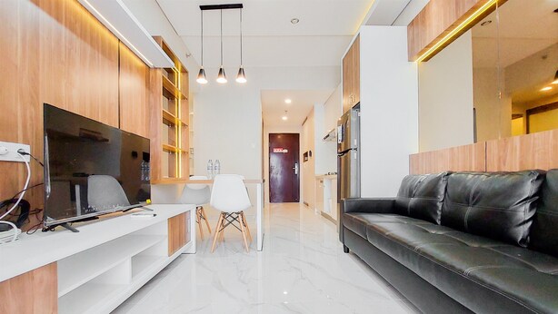 A modern living room with a black leather sofa, wooden cabinets, a flat-screen TV, and a dining area with a white table and chairs. - Well Designed And Comfy 2Br Sky House Bsd Apartment (Pagedangan)