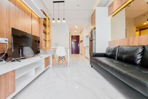 A modern living room with a black leather sofa, wooden cabinets, a flat-screen TV, and a dining area with a white table and chairs. - Well Designed And Comfy 2Br Sky House Bsd Apartment (Pagedangan)