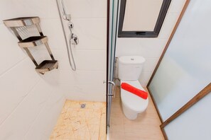 A bathroom with a shower, toilet, and a shelf unit. - Well Designed And Comfy 2Br Sky House Bsd Apartment (Pagedangan)