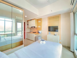 Quarto de hotel com cama, cozinha compacta, televisão e uma janela grande.