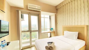 Una habitación de hotel con cama, escritorio con televisor, ventana con vistas y aire acondicionado.