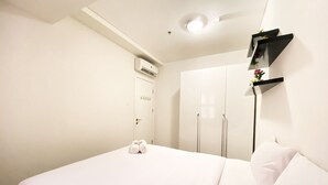 A hotel room with a bed, a wardrobe, an air conditioning unit, and a shelf with a plant. - Comfy And Modern 2Br Apartment At Parahyangan Residence (Bandung)