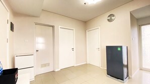 A spacious room with white walls, a tiled floor, and a black refrigerator. There are three white doors and a clock on the wall. - Comfy And Modern 2Br Apartment At Parahyangan Residence (Bandung)