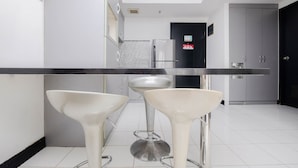 A modern kitchen with a black countertop, two white bar stools, a stainless steel refrigerator, and a black door in the background. - Nice And Elegant 1Br At The Wave Kuningan Apartment (Jakarta)