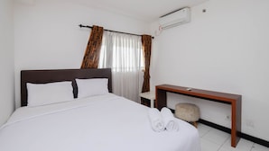 A neatly made bed with white linens, a wooden nightstand with a lamp, and a small round stool. - Nice And Elegant 1Br At The Wave Kuningan Apartment (Jakarta)