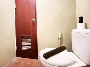 A bathroom with a white toilet, a brown door, and a white toilet paper holder. - Warm And Cozy Studio At Taman Melati Jatinangor Apartment (Hegarmanah)