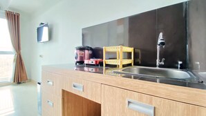 A modern kitchen with wooden cabinets, a stainless steel sink, and a compact refrigerator. - Warm And Cozy Studio At Taman Melati Jatinangor Apartment (Hegarmanah)